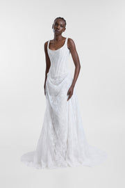 A model wearing the Joni Gown, a floor-length ivory corded lace A-line wedding dress with a corseted bodice, scoop neckline, shoulder straps, and a draped skirt.