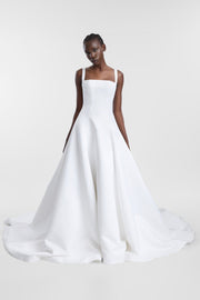 A model wearing the Holloway Gown, a bright ivory satin A-line gown with a square neckline, wide straps and a full structured skirt.