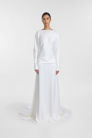 A model wearing the Lola Gown, a floor-length ivory satin wedding dress with long sleeves and a relaxed silhouette, photographed against a seamless light gray studio background.