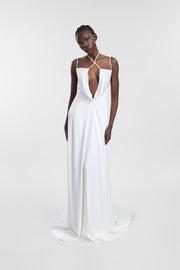 A model wearing the Isabel Gown, a floor-length ivory double satin wedding dress featuring a low cowl neckline with natural pearl detailing, an open back, and a fluid, relaxed skirt.