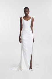A model wearing the Estel Gown, a floor-length ivory satin wedding dress with a scoop neckline, asymmetric draping and a thigh-high side slit.