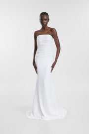 A model wearing the Pepe Gown, a floor-length ivory strapless wedding dress with horizontal draping, a fitted silhouette and softly flared hem.