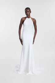 A model wearing the Piero Gown, a white floor-length gown with a high halter neckline, fitted silhouette and soft flared hem.