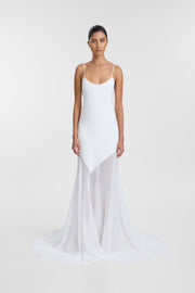 A model wearing the Parella Gown, an ivory scoop-neck gown with thin straps, a fluid silhouette and sheer chiffon scarf detailing at the hem.