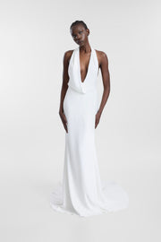 A model wearing the Armada Gown, a white floor-length gown with a plunging halter neckline and fitted, gently flared silhouette.